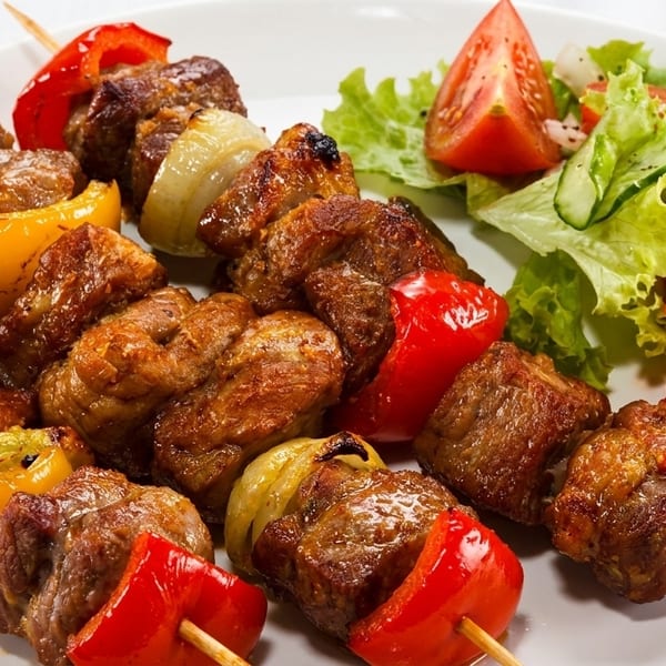 Grilled meat and vegetable skewers with a side salad of lettuce, tomatoes, and cucumbers.